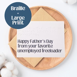 May include: A white Father's Day card with braille and large print, featuring the message "Happy Father's Day from your favorite unemployed freeloader." The card is on a wooden tray with a brown envelope.