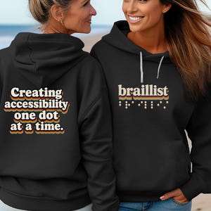 May include: A black hooded sweatshirt featuring the text "braillist" with Braille dots below it on the front, and the text "Creating accessibility one dot at a time." on the back. The lettering uses a retro-style multi-colored layered font design.