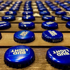 May include: A close-up of a wooden surface with a pattern of stars. The surface is covered with blue and white Bud Light bottle caps. The caps are arranged in rows and columns, creating a visual pattern.