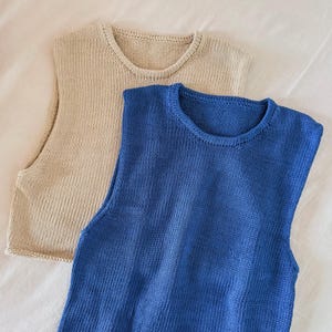 May include: Two knitted sleeveless tops. One is a light beige color, and the other is a vibrant blue. Both tops have a crew neck and a simple, classic design. The fabric appears to be a soft, breathable knit, perfect for layering or wearing on its own.