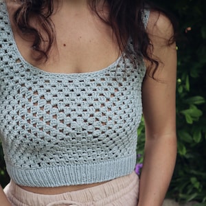 May include: A light blue crochet crop top with a square stitch pattern. The top is sleeveless and has a scoop neck.