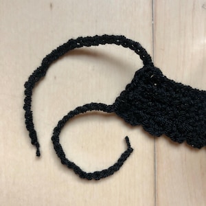 May include: A black crocheted headband with a loose end of yarn.