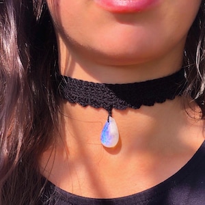Può includere: Un girocollo in pizzo nero con un ciondolo a forma di lacrima in pietra preziosa iridescente.