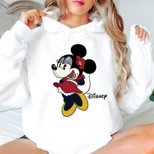 Puede incluir: Sudadera con capucha blanca con una imagen de dibujos animados de Minnie Mouse con un vestido rojo y zapatos amarillos. El texto "DISNEY" est&aacute; impreso debajo de la imagen.