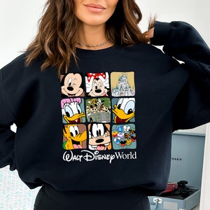 Op de afbeelding: Zwart sweatshirt met een kleurrijke grafische print van verschillende Disney-figuren, waaronder Mickey Mouse, Minnie Mouse, Donald Duck, Goofy en het kasteel van Assepoester. De tekst "Walt Disney World" is onder de print gedrukt.