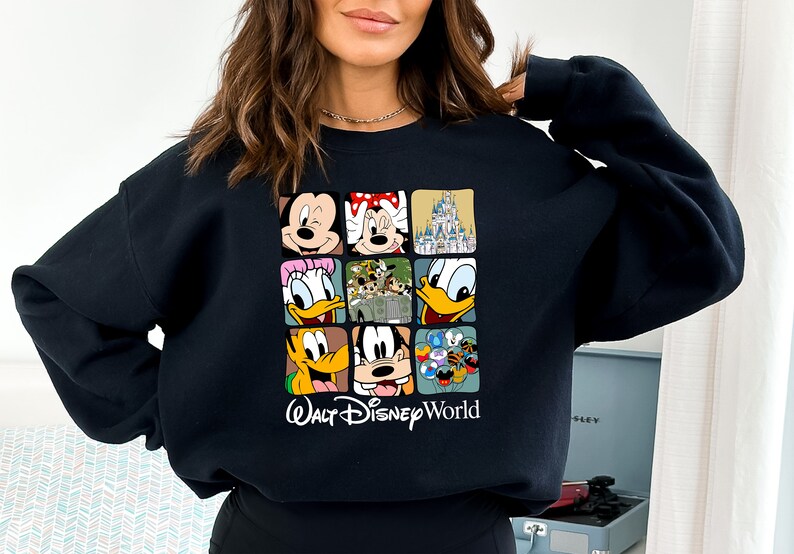 Op de afbeelding: Zwart sweatshirt met een kleurrijke grafische print van verschillende Disney-figuren, waaronder Mickey Mouse, Minnie Mouse, Donald Duck, Goofy en het kasteel van Assepoester. De tekst "Walt Disney World" is onder de print gedrukt.