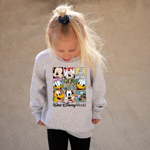 Op de afbeelding: Een grijs longsleeve sweatshirt met een kleurrijke afbeelding van Mickey Mouse, Minnie Mouse, Donald Duck, Goofy en het kasteel van Assepoester. De tekst "Walt Disney World" staat onder de afbeelding.
