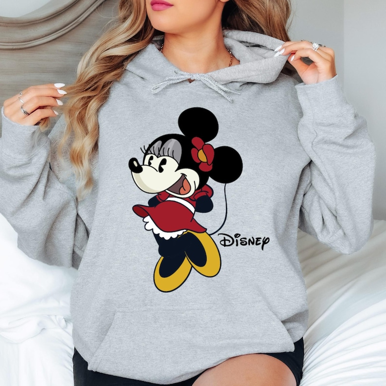 Puede incluir: Sudadera gris con capucha con una imagen de dibujos animados de Minnie Mouse con un vestido rojo y un lazo rojo. El texto "DISNEY" est&aacute; impreso debajo de la imagen.