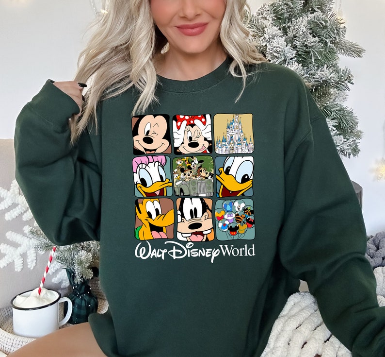 Op de afbeelding: Een donkergroen sweatshirt met een grafische print van verschillende Disney-figuren, waaronder Mickey Mouse, Minnie Mouse, Donald Duck, Goofy en Pluto. De grafiek bevat ook het iconische kasteel van Assepoester en de tekst "Walt Disney World".