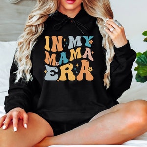 Pu&ograve; includere: Felpa con cappuccio nera con il testo "In My Mama Era" in lettere retr&ograve; colorate con stelle e fiori.