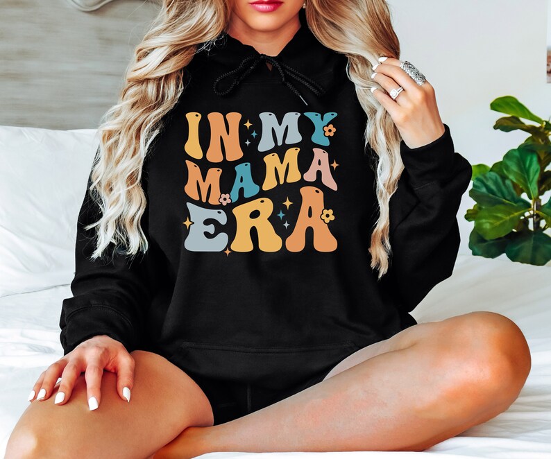 Pu&ograve; includere: Felpa con cappuccio nera con il testo "In My Mama Era" in lettere retr&ograve; colorate con stelle e fiori.