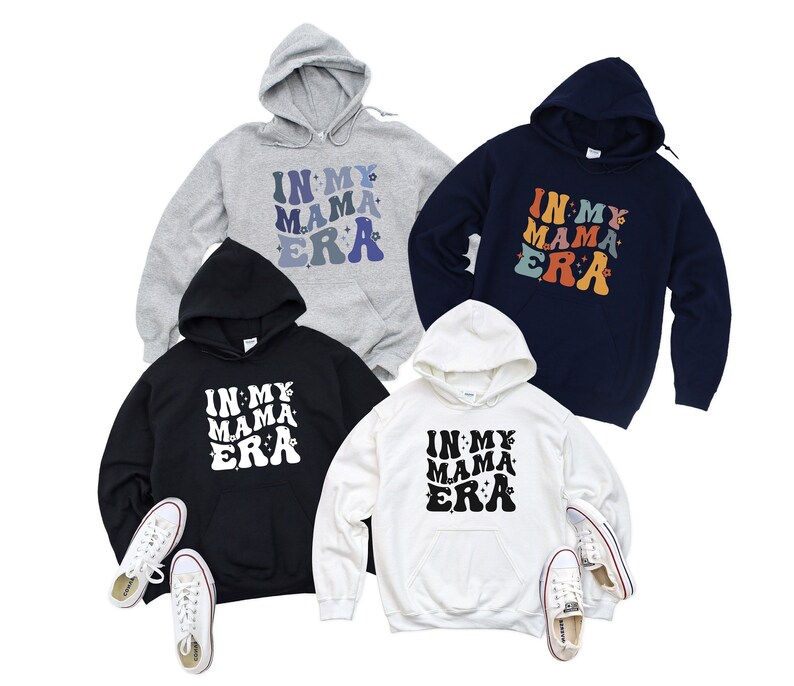 Pu&ograve; includere: Quattro felpe con cappuccio di diversi colori con la scritta "In My Mama Era" stampata sul davanti. Le felpe sono di colore grigio, blu navy, nero e bianco.
