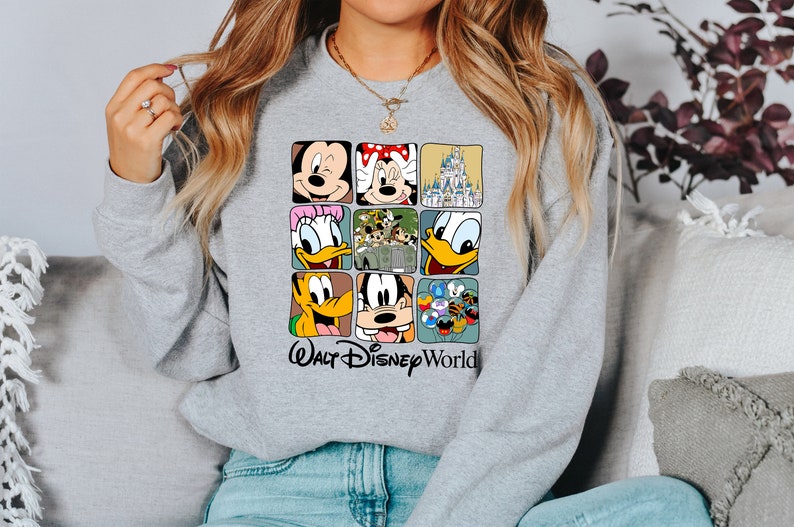 Op de afbeelding: Grijs sweatshirt met een grafische print van verschillende Disney-figuren, waaronder Mickey Mouse, Minnie Mouse, Donald Duck, Goofy en het kasteel van Assepoester. De tekst "Walt Disney World" is onder de print gedrukt.