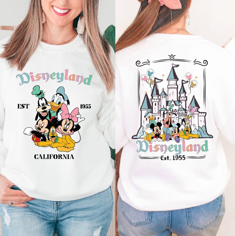 May include: White sweatshirt with a colourful Disneyland graphic featuring Mickey Mouse, Minnie Mouse, Donald Duck, Goofy, and Pluto. The front of the sweatshirt says "Disneyland EST 1955 CALIFORNIA" and the back of the sweatshirt says "Disneyland Est. 1955" with a colourful illustration of Sleeping Beauty's castle.
