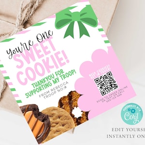 May include: A pink and white card with the text "You're One SWEET COOKIE!" and "THANK YOU FOR SUPPORTING MY TROOP!" is displayed. A green bow and a QR code are also visible. The card is next to a box with cookies.