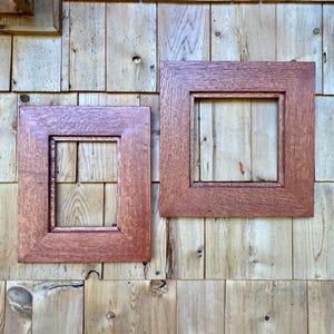 May include: Two rectangular wooden picture frames with a reddish-brown finish and a visible wood grain texture. One frame is oriented vertically, while the other is square, both featuring a beveled inner edge design.