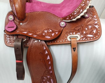 Könnte beinhalten: Ein brauner Ledersattel mit rosa Wildledersitz und floralem Werkzeug. Der Sattel verfügt über einen silbernen Concho und einen rosa Steigbügel.