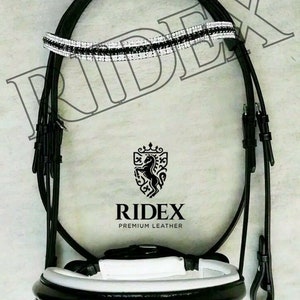 Puede incluir: Bridón de cuero negro para caballo con frontal acolchado blanco y frontal de cristal blanco y negro. El bridón tiene el logotipo "Ridex Premium Leather" en la nariz.