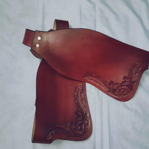 May include: Two burgundy leather boot cuffs with floral tooling. The cuffs are made of thick leather and have a decorative design.