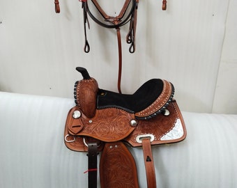 May include: A brown leather saddle with silver accents and a black seat. The saddle is hanging on a wall with a matching brown leather bridle.