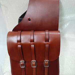 May include: A brown leather saddlebag with three buckles and straps. The bag has a flap that folds over the top and is secured with a buckle.