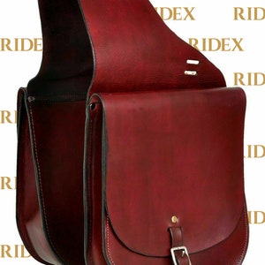 May include: A burgundy leather saddle bag with a flap closure and a buckle. The bag has two compartments and a strap for carrying.