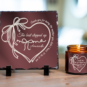 May include: A maroon slate plaque with white text and a heart design, along with a lit candle in a glass jar. The plaque reads "Thank you for being the mother you didn't have to be to me. The best stepped up mom Amanda." The candle has a matching label.