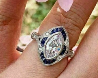 May include: A silver ring with a large marquise-shaped diamond surrounded by a halo of smaller diamonds and blue sapphires.