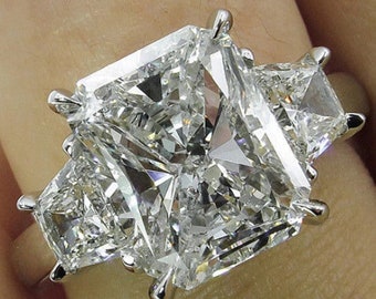 May include: A three-stone diamond engagement ring with a large, rectangular-shaped center stone and two smaller, triangular-shaped side stones.