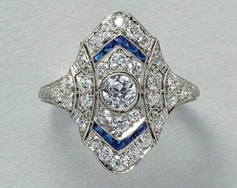 May include: A vintage-style ring with a large, round, clear center stone surrounded by smaller diamonds and blue sapphires. The ring is set in a silver band.