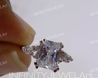 Puede incluir: Un anillo de plata con una gran piedra preciosa cuadrada transparente. El anillo está engastado con piedras preciosas transparentes más pequeñas en la banda.