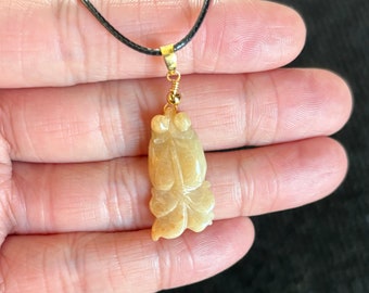 Puede incluir: Un collar con un colgante de jade tallado en forma de dos figuras. El colgante es de color amarillo claro y tiene un diseño detallado.