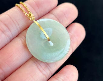 Op de afbeelding: Een lichtgroene jade hanger in de vorm van een cirkel met een gouden beugel. De hanger hangt aan een gouden ketting.