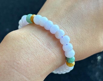 May include: A lavender jade bracelet with green and yellow jade accents. The bracelet is made of round beads and is worn on a person's wrist.