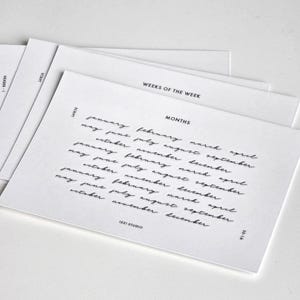 May include: A stack of white rectangular cards featuring black printed text. The top card displays the word MONTHS in a sans-serif font above a list of months written in a cursive script. The text 1521 STUDIO and SS-1A are printed at the bottom.