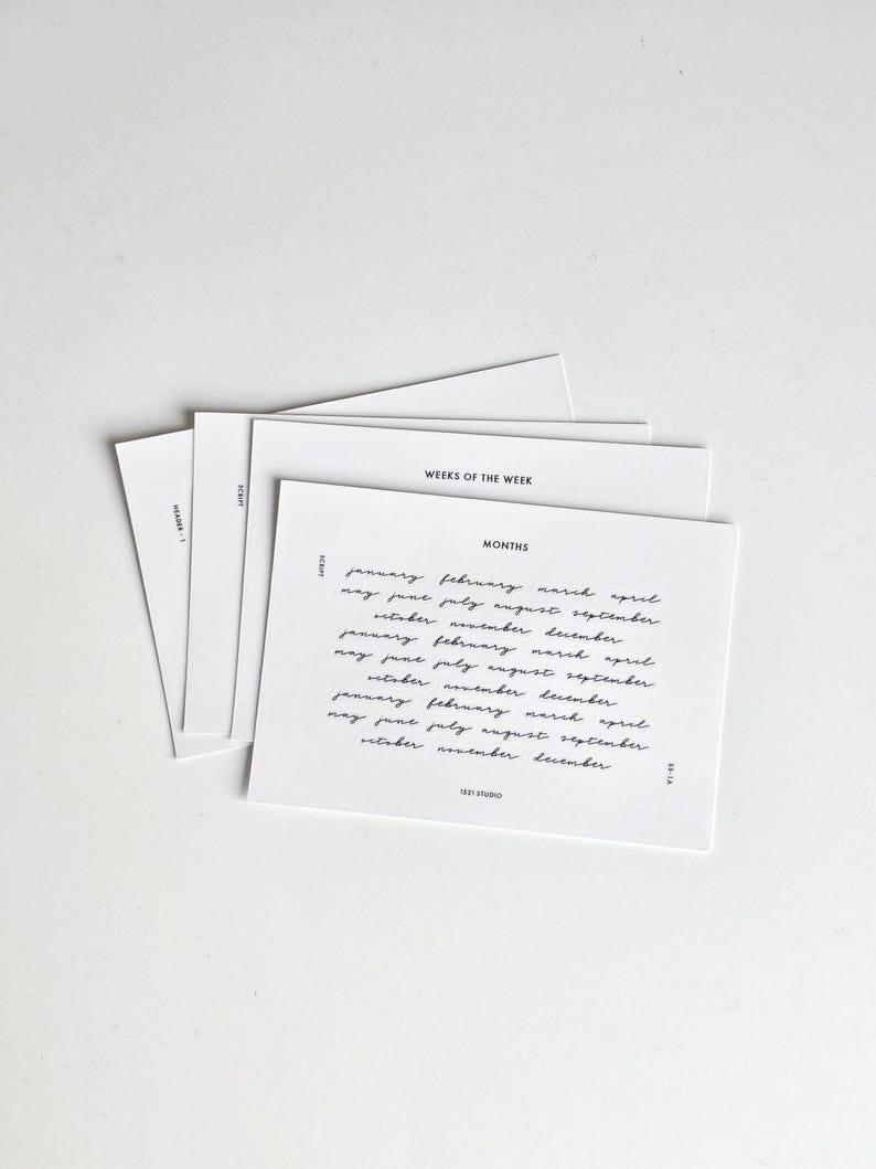 May include: A stack of white rectangular cards with black text. The top card features the heading MONTHS followed by a list of months in a cursive script font. Other visible text includes WEEKS OF THE WEEK, SCRIPT, HEADER 1, 1531 STUDIO, and 22-1A.