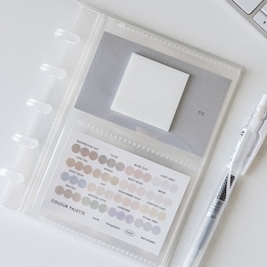 Könnte beinhalten: Ein durchsichtiger Plastikordner mit einer Farbpalette, die 15 verschiedene Farbtöne in Beige, Rosa und Lila zeigt. Die Farbpalette ist mit "COLOUR PALETTE" beschriftet und enthält Namen für jede Farbe, wie z. B. "Mushroom Cap", "Chai Tea", "Taupe" und "Rose Clay".