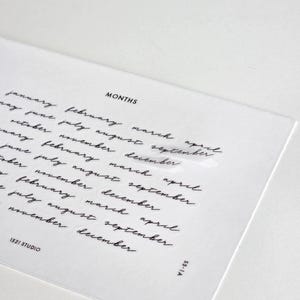 May include: A clear rectangular sticker sheet featuring the word MONTHS in a bold sans-serif font at the top, followed by multiple rows of the twelve months of the year written in a black cursive script. The bottom corners display 1521 STUDIO and SS-1A.
