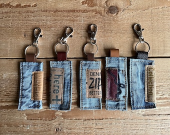 May include: Five denim keychains with different fabric patches and text. The patches include "here +", "DENIM ZIP BETTER", "Collection", and two other patches with unreadable text.