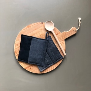 Puede incluir: Dos agarraderas de tejido gris oscuro con una cuchara de madera en una tabla de cortar redonda de madera.