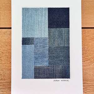 May include: A white framed print with a geometric design made of different shades of blue denim fabric. The print is signed "Ioana Weber" in the bottom right corner.