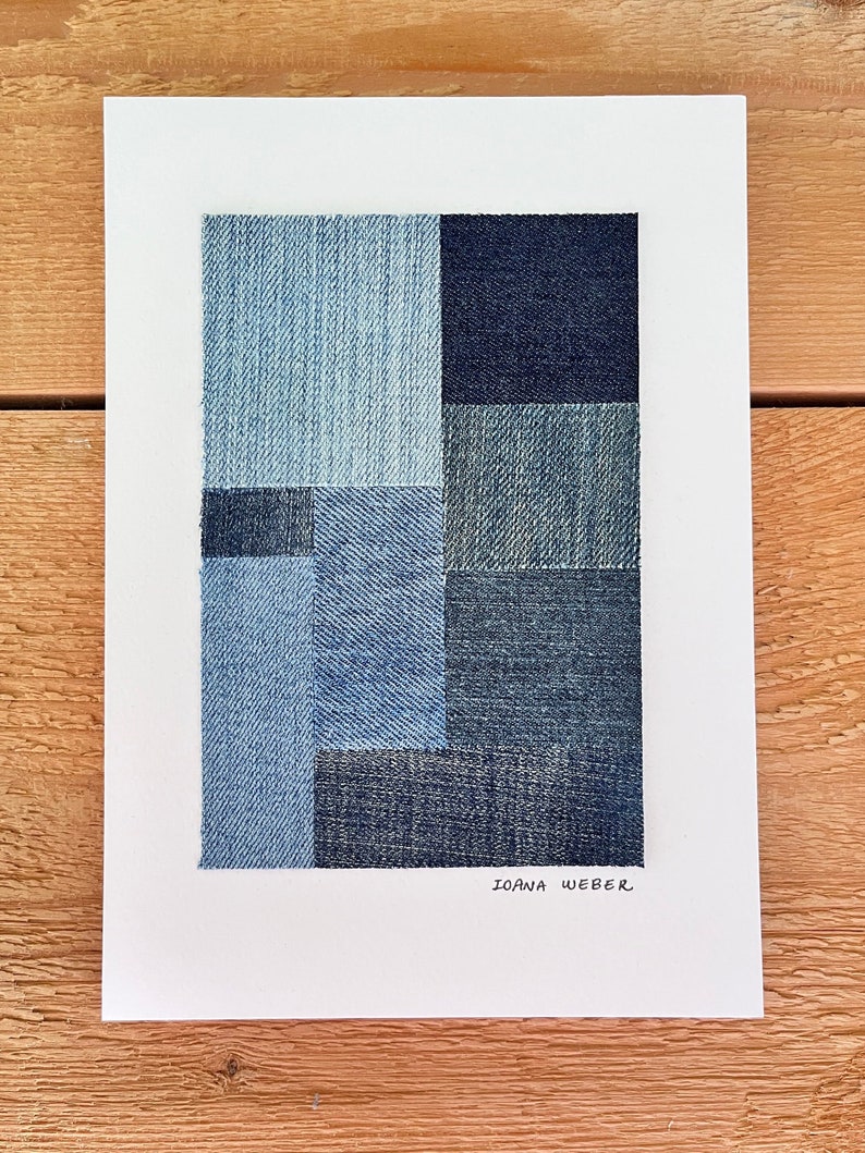 May include: A white framed print with a geometric design made of different shades of blue denim fabric. The print is signed "Ioana Weber" in the bottom right corner.
