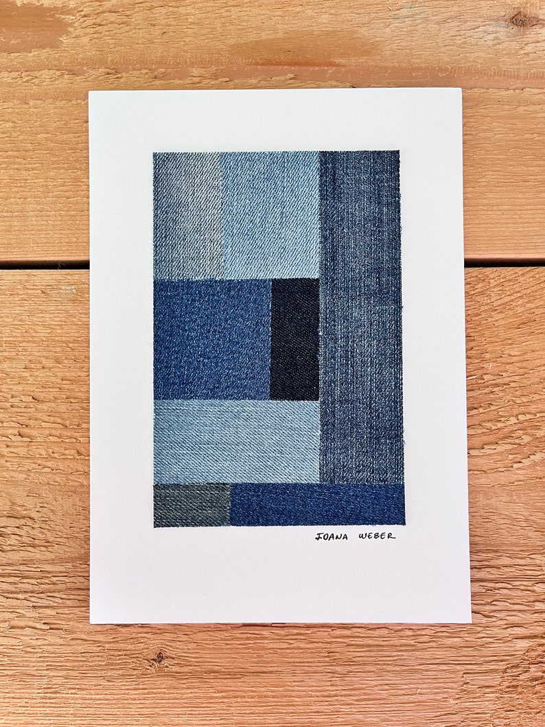 May include: Abstract art print featuring a geometric design made of different shades of blue denim fabric. The print is signed "JOANA WEBER" in the bottom right corner.