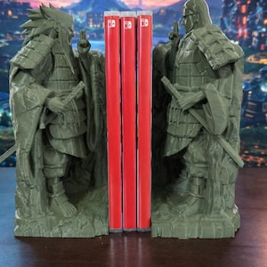 May include: Olive-green statue bookends, each depicting a figure in traditional dress, framing three red game cartridges. The background shows a blurred night sky and a cityscape.