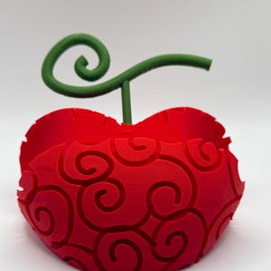 May include: A red 3D printed model of a fruit with a green stem and a swirl pattern. The fruit is shaped like a heart and has a textured surface.
