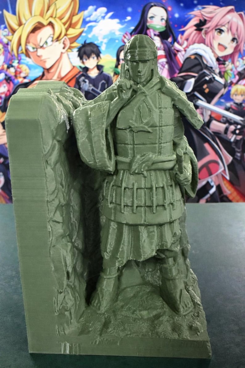 May include: A green 3D-printed figurine of a warrior in armour, standing on a rocky base. The figure is detailed with segmented armour, a helmet, and a sword. The background features colourful anime-style characters.