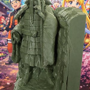 May include: A green figurine of a character in a traditional Japanese outfit, with a hand raised to the mouth. The figure is set against a backdrop of anime characters and a Japanese festival scene with lanterns and cherry blossoms.