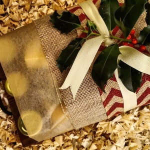 May include: A gift basket wrapped in burlap fabric with a red and white chevron pattern. The basket is tied with a white ribbon and decorated with holly and red berries.