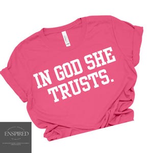 Può includere: Maglietta rosa con testo bianco che recita "In God She Trusts."