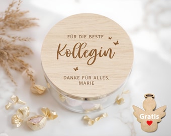 May include: A wooden box with a lid that says "For the best colleague, thank you for everything, Marie". The lid is decorated with butterflies. The box is filled with small, round candies.